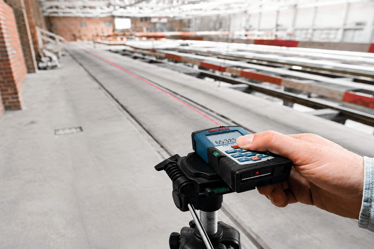 Handheld laser distance meter measuring a long distance inside an industrial workshop